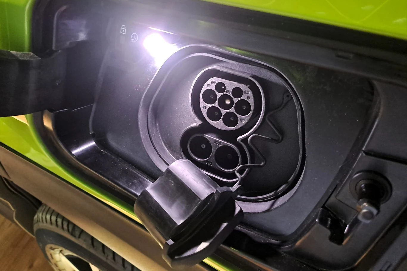 Gniazdo ładowania samochodu elektrycznego w jasnozielonym pojeździe. Widoczne są elementy złączy ładowarki oraz osłona gniazda.