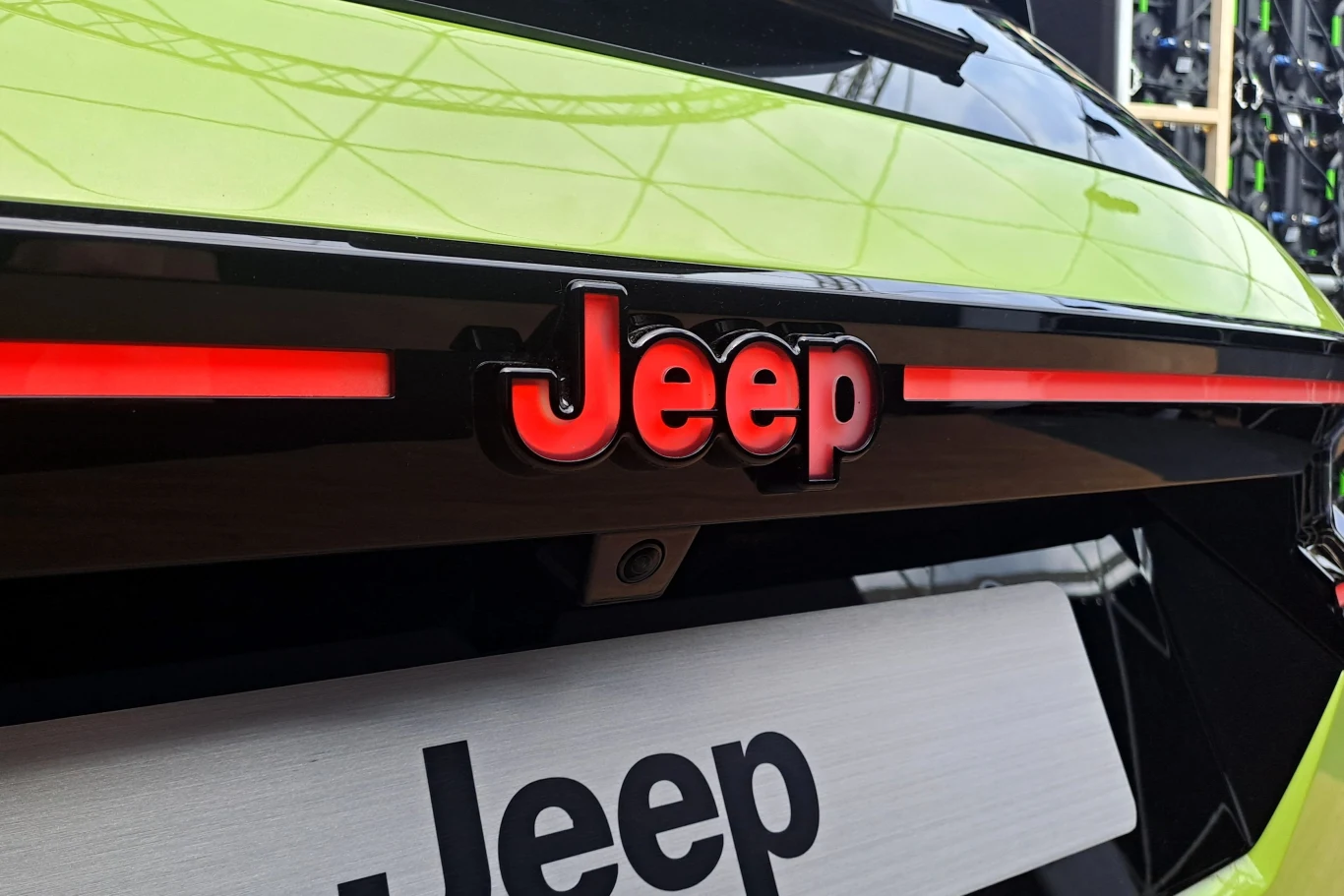 Logo Jeepa na tylnej części karoserii samochodu w kolorze limonkowym, z czerwonymi detalami oświetlenia akcentującymi logo.