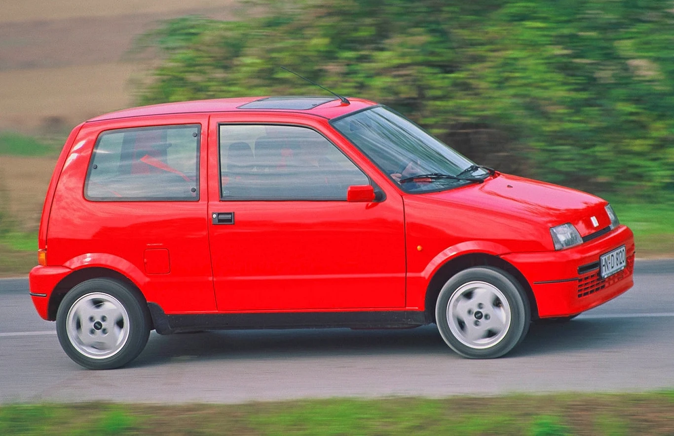 Po blisko 40 latach Włosi kończą produkcję rodziny silników FIRE. Napędzały niezliczone modele Fiata Jasnoczerwony samochód kompaktowy jadący po wiejskiej drodze, widoczny z boku na tle zieleni.