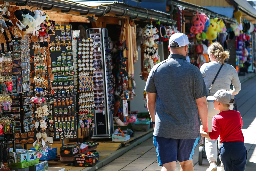 Krupówki nie zawsze były tak skomercjalizowane Kiosk z pamiątkami pełen kolorowych zabawek i gadżetów, z parą dorosłych i dzieckiem spacerującymi wzdłuż straganu.