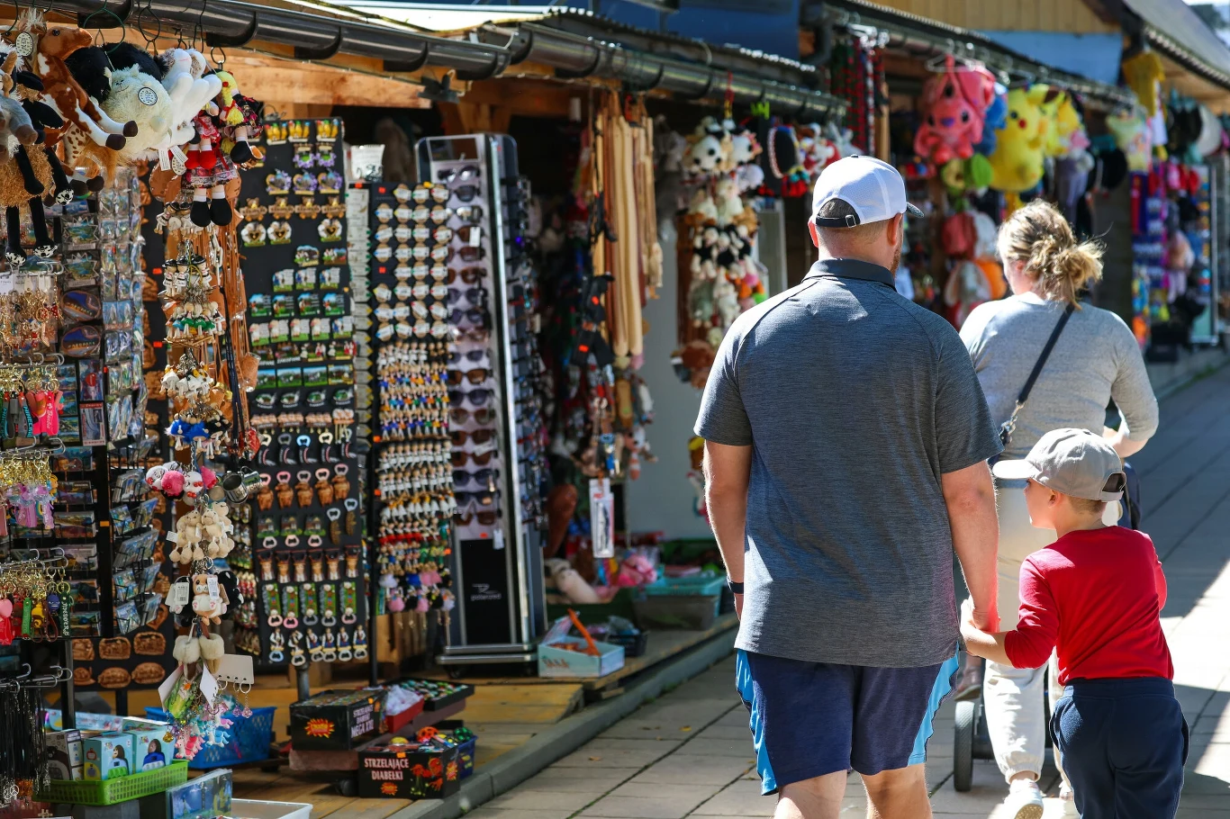 Kiosk z pamiątkami pełen kolorowych zabawek i gadżetów, z parą dorosłych i dzieckiem spacerującymi wzdłuż straganu.