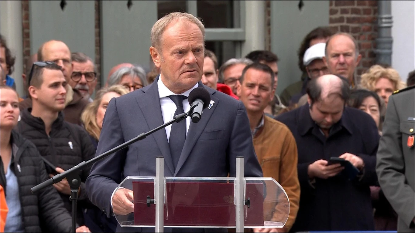 Donald Tusk zabrał głos podczas obchodów Dnia Wyzwolenia Holandii Osoba w eleganckim garniturze przemawia przez mikrofon na tle grupy ludzi. W tle widać różnorodną publiczność, która uważnie słucha lub zajmuje się swoimi sprawami.
