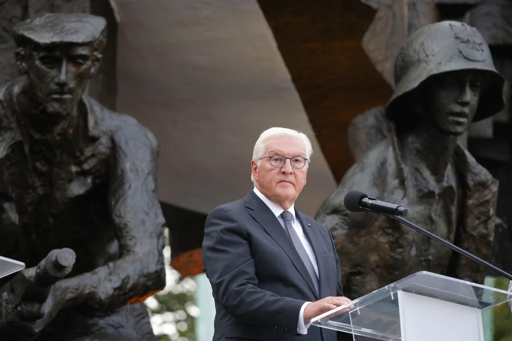 Prezydent Niemiec Frank-Walter Steinmeier podczas obchodów 80. rocznicy Powstania Warszawskiego Mężczyzna w garniturze przemawia przy mównicy na tle pomnika, na którym widnieją postacie żołnierzy. W tle znajduje się rzeźba przedstawiająca żołnierzy w wojskowych mundurach i hełmach.