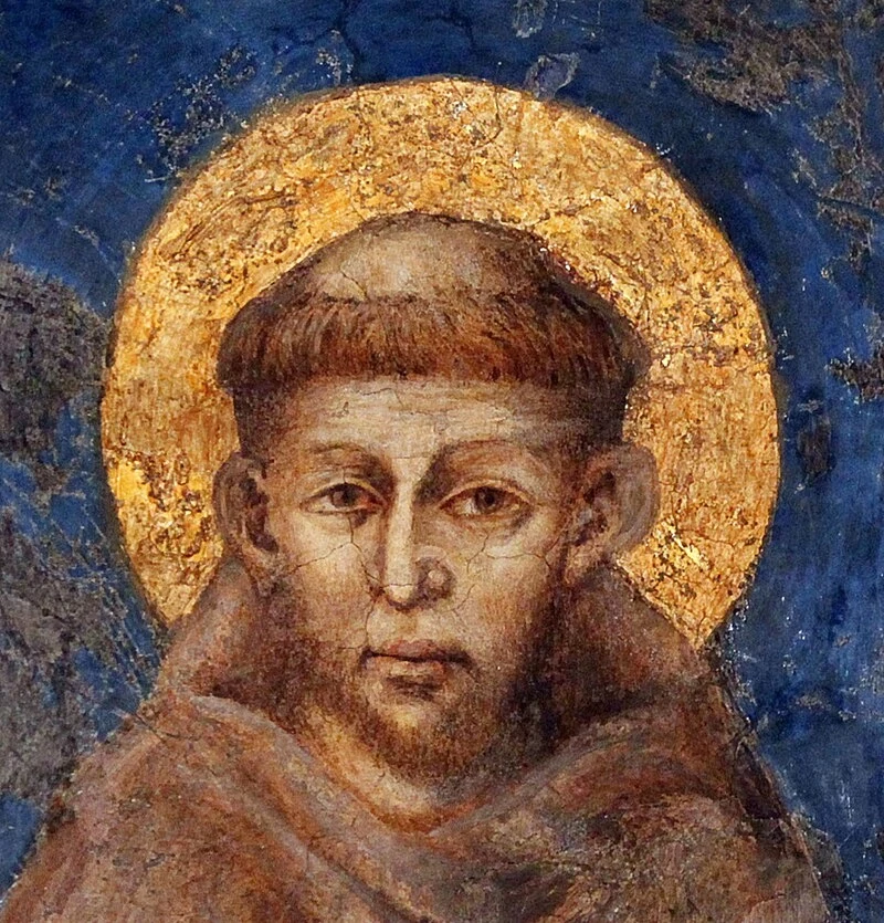 Święty Franciszek z Asyżu – symbol prostoty, pokoju i troski o ubogich. Jego imię wybrał papież Franciszek, nadając swojemu pontyfikatowi wyraźny kierunek. /domena publiczna Święty Franciszek przedstawiony jako postać z aureolą, ubrana w prosty, ciemny habit, na tle niebieskiej ściany ze złotymi elementami. Obraz cechuje się delikatnym, realistycznym stylem malarskim.