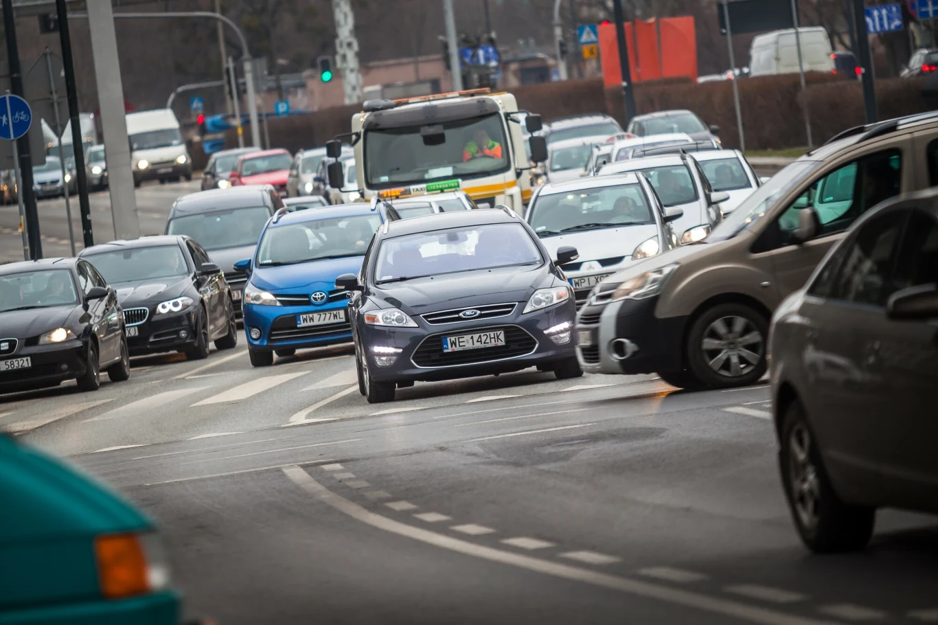Stosowanie tak zwanego wachlarzyka pozwala upłynnić ruch na skrzyżowaniach Intensywny ruch uliczny na miejskiej drodze z wieloma samochodami osobowymi i dostawczymi. W tle można dostrzec sygnalizację świetlną oraz miejską infrastrukturę drogową. Widoczny korek tworzy atmosferę zgiełku i codziennego pośpiechu.