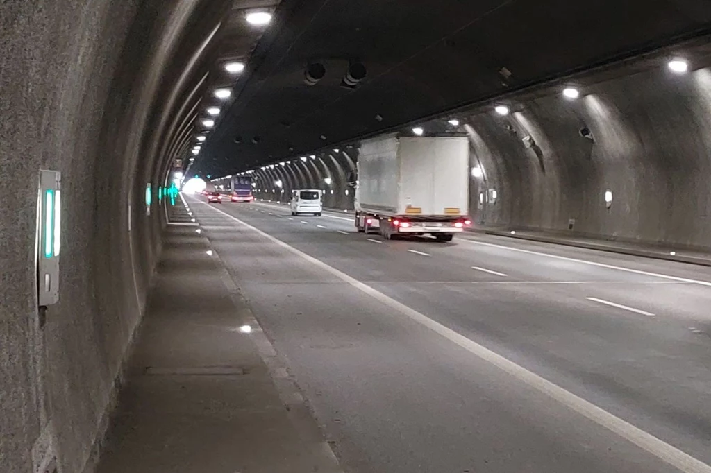 1 maja 2025 r. padł tegoroczny rekord dziennej liczby pojazdów przejeżdżających tą trasą - tunel pokonało wówczas 42 020 pojazdów. Samochody poruszające się w tunelu autostradowym, widoczny pojazd ciężarowy oraz samochód osobowy jadące w tym samym kierunku. Oświetlenie tunelu tworzy regularny wzór na suficie i ścianach, a w oddali widać wylot tunelu.