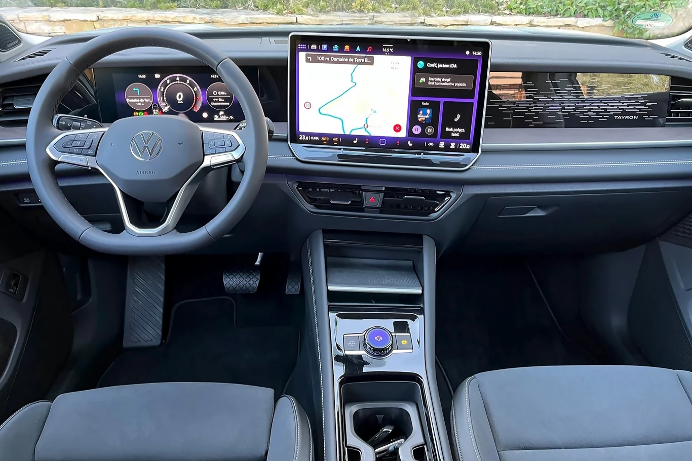 Do zalet testowanego modelu należy precyzyjnie działający układ kierowniczy oraz doskonałe wyciszenie wnętrza. Wnętrze nowoczesnego samochodu marki Volkswagen z widocznym kokpitem i dużym ekranem dotykowym na środku deski rozdzielczej. Po lewej stronie znajduje się kierownica z logo producenta, a na ekranie widoczna jest mapa nawigacyjna.