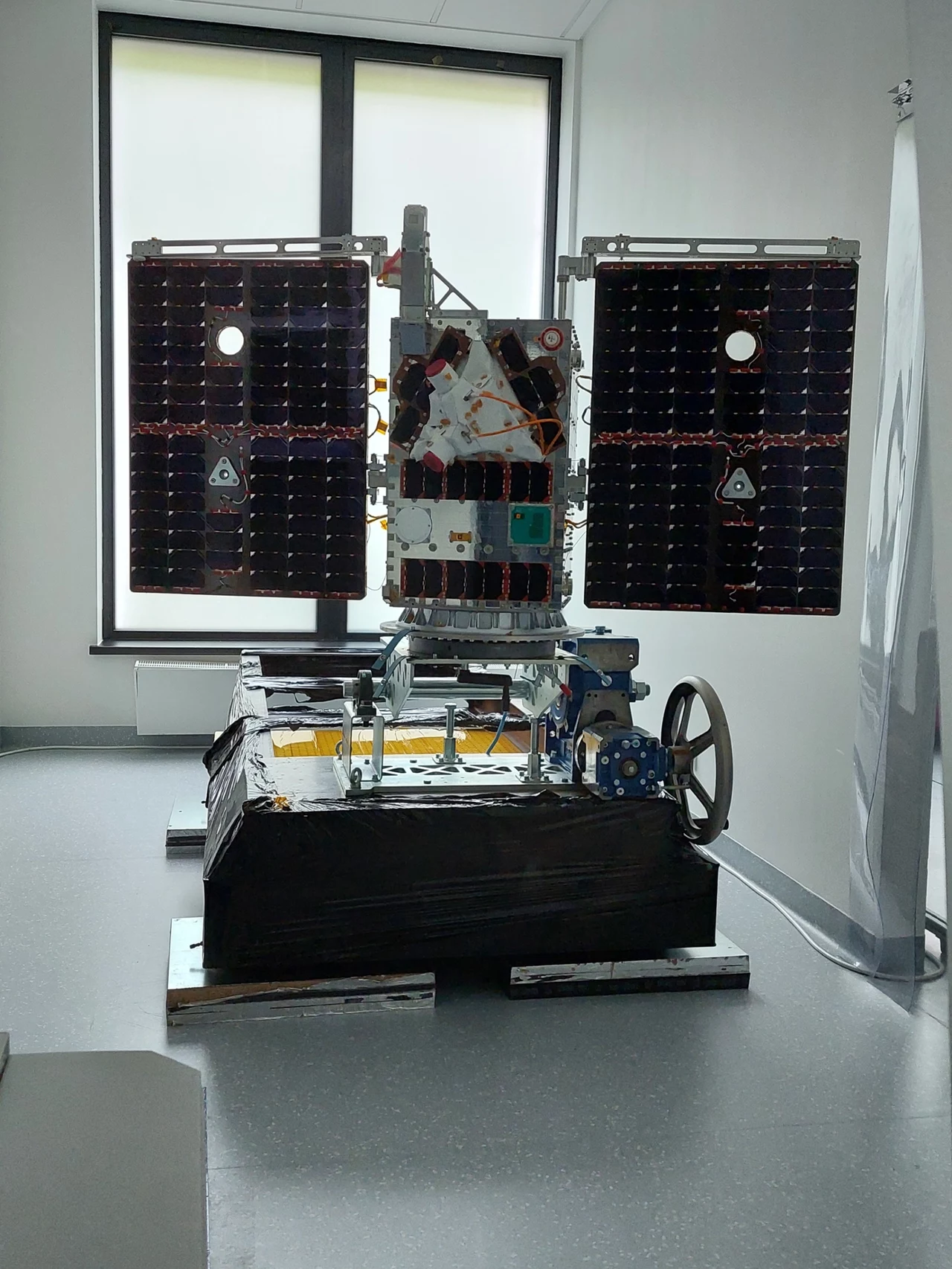 Polski satelita EagleEye przed lotem w kosmos w 2024 roku. Model satelity znajdujący się w nowoczesnym pomieszczeniu, z wyraźnie widocznymi panelami słonecznymi oraz różnymi elementami technicznymi, umieszczony na podstawie.