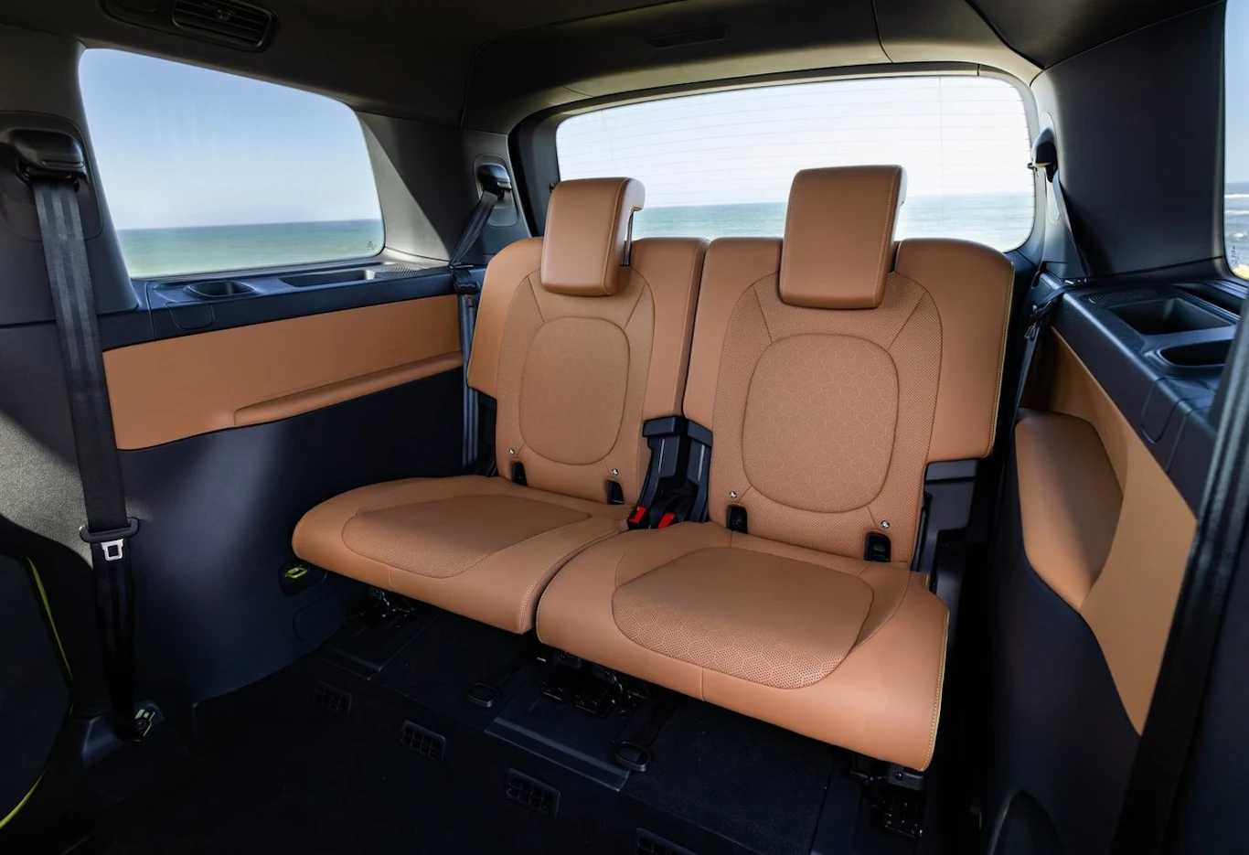 Wnętrze samochodu z widokiem na tylne siedzenia wykonane z brązowej tapicerki. Widać dwa rozłożone fotele oraz widok za oknem na horyzont.