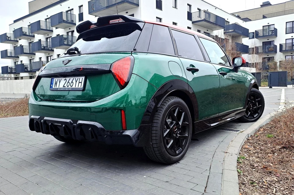 Testowana przez nas specyfikacja spalinowego Coopera to wersja S. Dwulitrowy silnik generuje 204 KM i 300 Nm. Zielony, sportowy samochód zaparkowany na kostce brukowej na tle nowoczesnego budynku mieszkalnego. Auto wyróżnia się nowoczesnym, dynamicznym designem oraz ciemnymi felgami.
