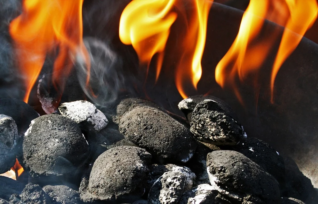 Fot. pixabay.com/ Bluesnap/ Płonące węgle w wysokiej temperaturze z widocznymi płomieniami i dymem unoszącym się w powietrzu.