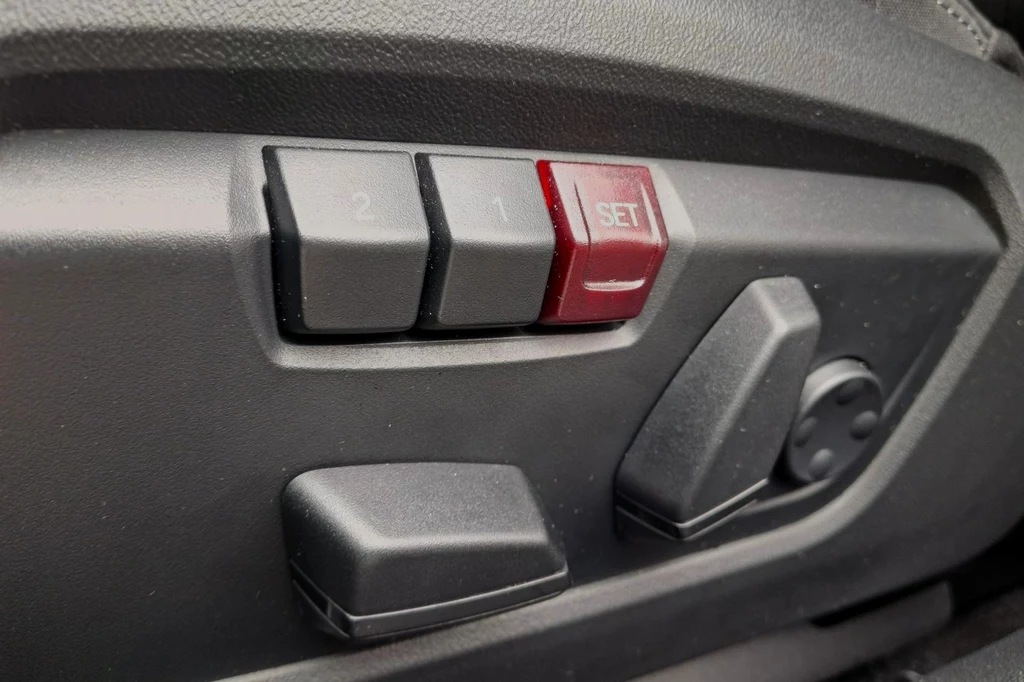 Fotele mogą oferować elektryczną regulację i pamięć ustawień (funkcja niedostępna w wariancie elektrycznym). Przyciski do regulacji fotela samochodowego, w tym przyciski do zapamiętywania ustawień 1 i 2 oraz przycisk SET. Widoczne także dźwignie do regulacji w pionie i poziomie.