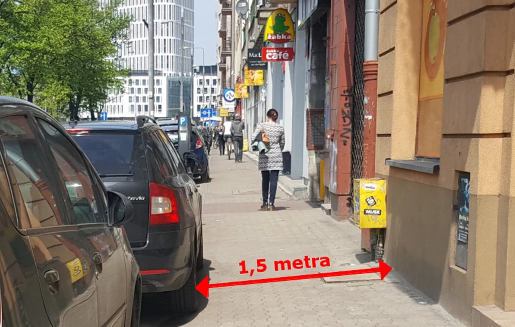 Kierowcy parkujący na chodniku muszą zostawić 1,5 m dla pieszych Samochód zaparkowany na chodniku, ograniczający przestrzeń do chodzenia pieszym. Ulica w tle z licznymi sklepami i reklamami oraz osoba idąca w oddali. Czerwona linia wskazuje odległość 1,5 metra między samochodem a ścianą budynku.