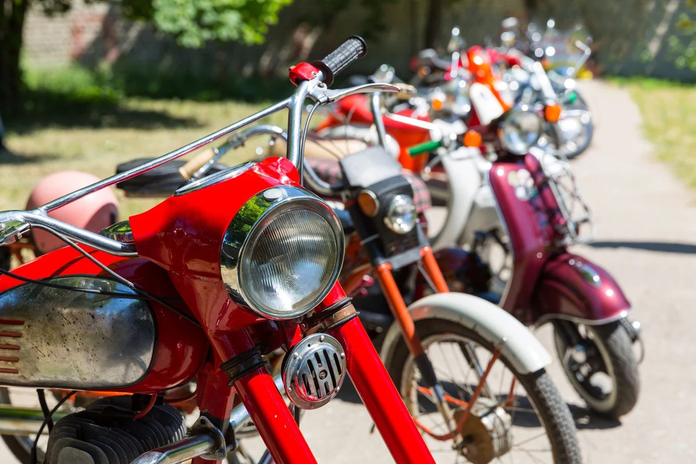 W Jadownikach od lat odbywają się motocyklowe pikniki. Rząd kolorowych, zabytkowych motocykli ustawionych na tle zieleni, z najbliższym planem skupionym na czerwonym motocyklu z chromowanymi detalami.