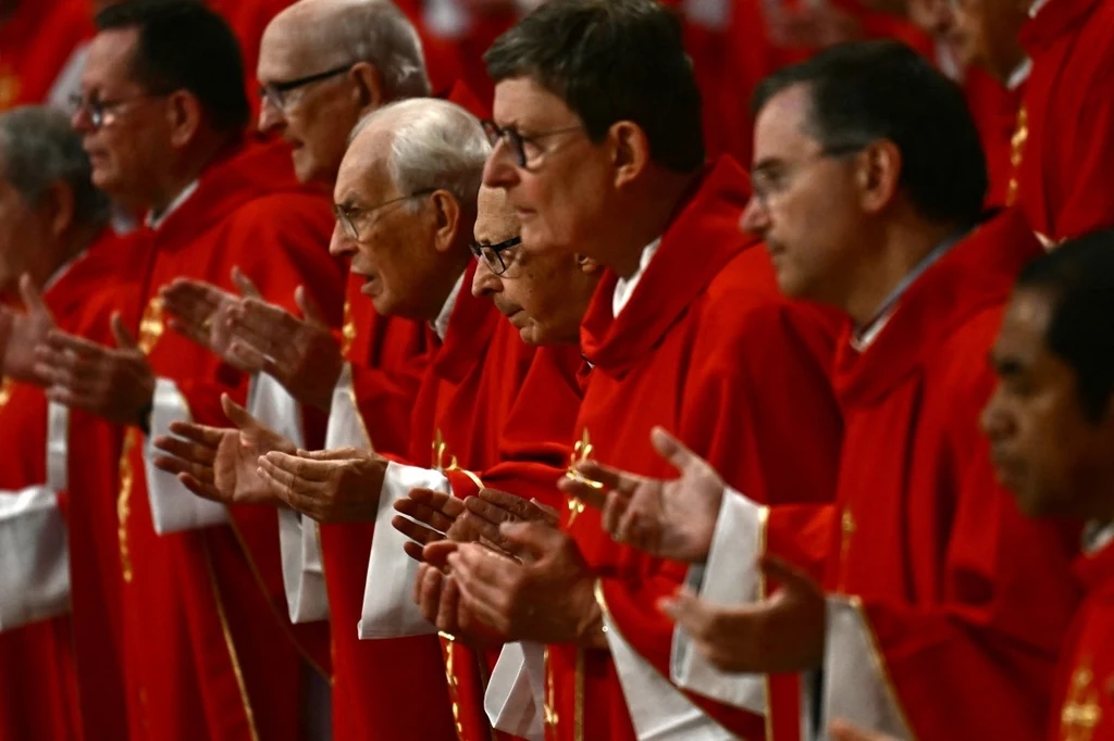 Kardynałowie przybyli do Watykanu podczas mszy Grupa duchownych ubranych w czerwone ornaty uczestniczących w ceremonii kościelnej, każdy z nich trzyma dłonie w geście modlitwy. Usiłując stworzyć atmosferę skupienia i duchowości, wszyscy są skierowani w jednym kierunku.