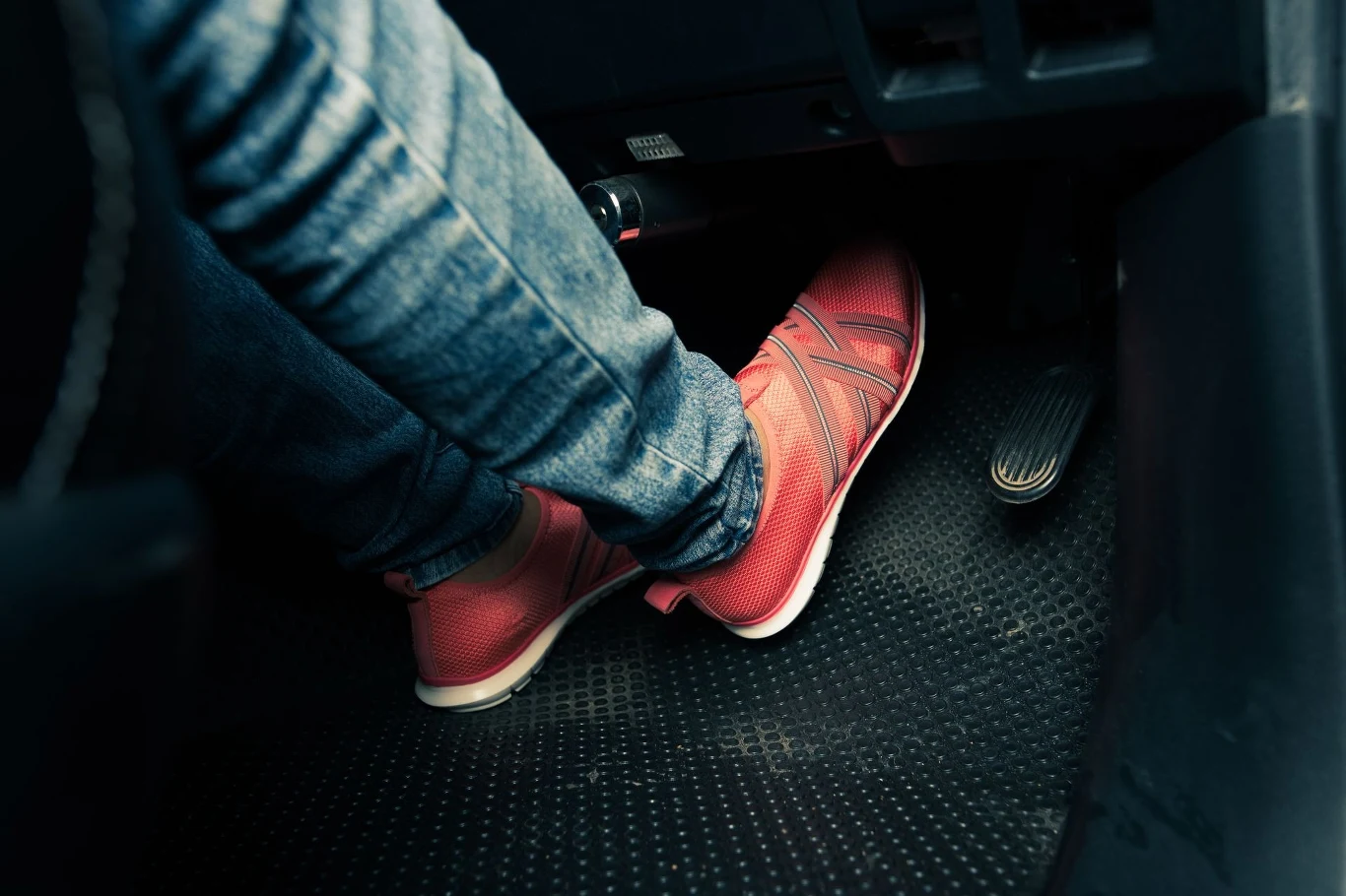 Funkcja Auto Hold jest obecna w wielu nowych autach. Kierowcy o niej nie wiedzą. Osoba w różowych butach na pedałach samochodu, ze szczególnym uwzględnieniem pedału przyspieszenia i hamulca, ubrana w jeansy.