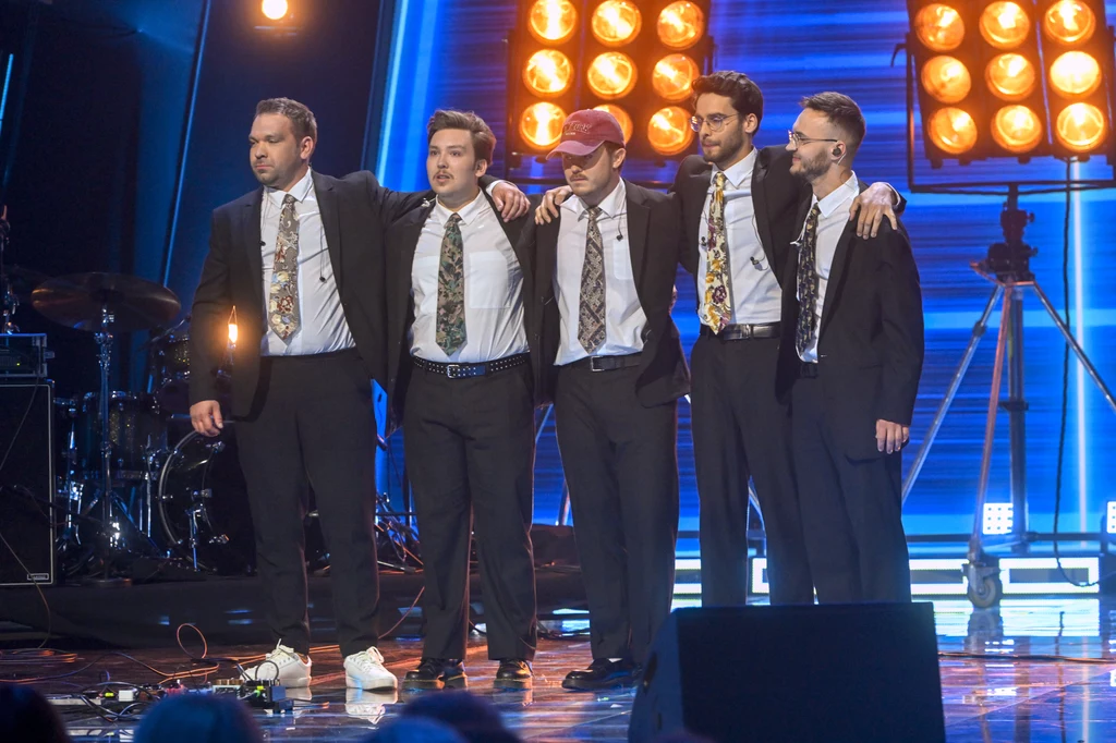Zespół Kuba i Kuba zakwalifikował się do finału "Must Be The Music" Grupa pięciu mężczyzn ubranych w garnitury i krawaty stoi razem na scenie w otoczeniu jasnych reflektorów i scenicznego sprzętu. Mężczyźni są obejmowani, a ich wygląd sugeruje występ lub wydarzenie publiczne.