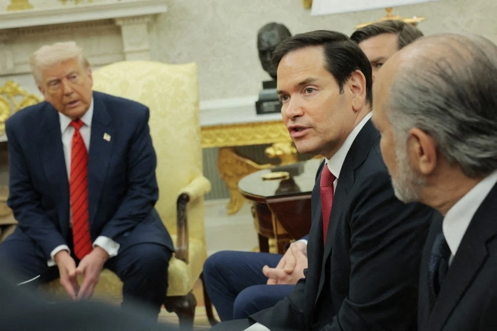 Sekretarz stanu USA Marco Rubio Politycy w formalnym otoczeniu prowadzą rozmowę. Jeden z nich siedzi na fotelu, drugi intensywnie gestykuluje, zwracając uwagę reszty uczestników. W tle eleganckie meble i dekoracje, które nadają scenie oficjalny charakter.
