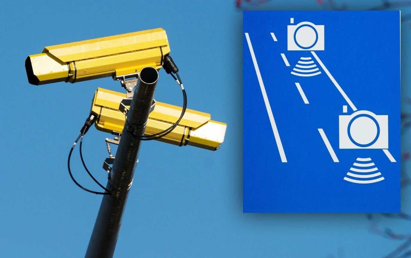 Zdjęcie przedstawia żółte kamery monitoringu zamontowane na słupie, symbolizujące nadzór i bezpieczeństwo. Obok widoczny jest niebieski znak drogowy z białym piktogramem przedstawiającym kamery monitoringu działające na drodze.