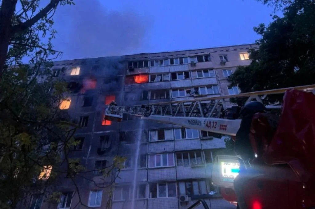W wyniku nocnego ataku na Kijów zginęły dwie osoby, a co najmniej siedem zostało rannych Pożar w wysokim budynku mieszkalnym, z widocznymi płomieniami i dymem wydobywającymi się z kilku okien. Na pierwszym planie drabina strażacka i wóz strażacki podświetlony migającymi światłami.