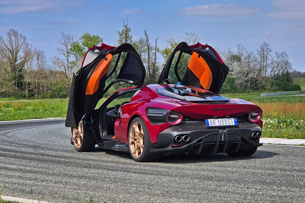 Alfa Romeo 33 Stradale Samochód sportowy z otwartymi drzwiami typu "motyl" na tle zielonego terenu poza miastem.