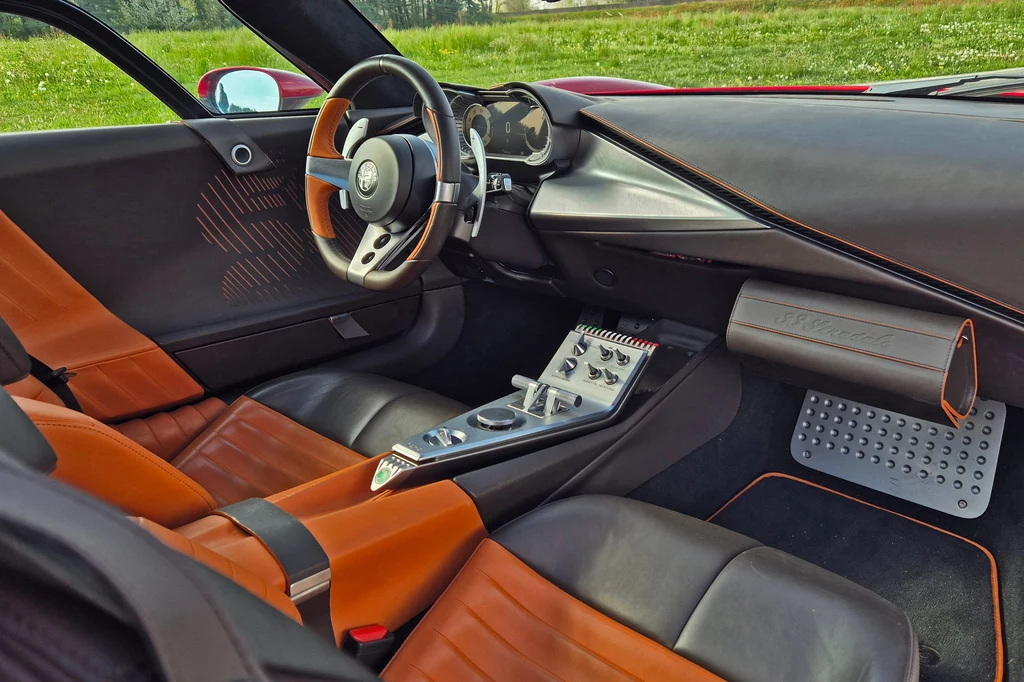 Alfa Romeo 33 Stradale Luksusowe wnętrze sportowego samochodu z czerwonym, skórzanym wykończeniem, nowoczesną deską rozdzielczą oraz wielofunkcyjną kierownicą. Widoczne elementy sterowania i panel audio. Przez okno widać zieleń na zewnątrz.