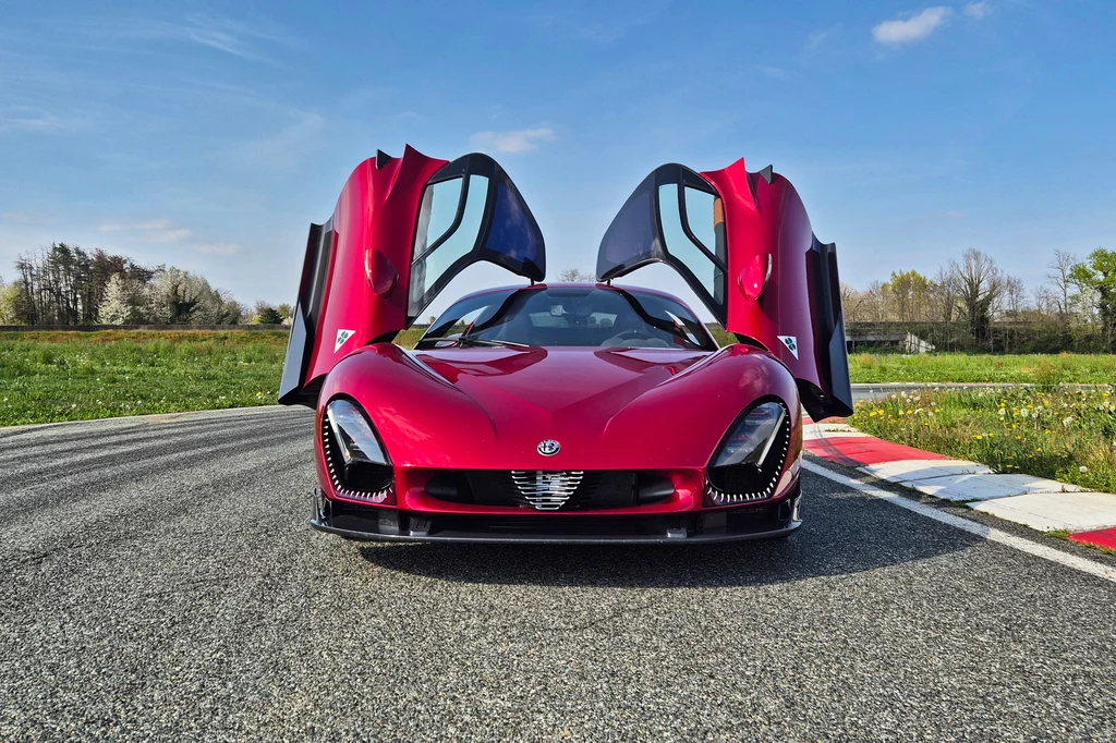 Alfa Romeo 33 Stradale Czerwony samochód sportowy z otwartymi drzwiami typu motyl, stojący na torze wyścigowym.