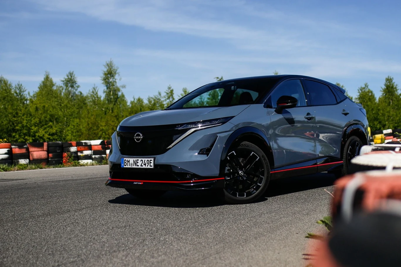 Samochód osobowy w sportowej wersji na torze wyścigowym, otoczony zielenią. Elegancki design pojazdu wyróżnia się na tle nieba i drzew.