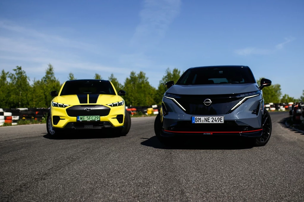 Ceny Nissana Ariyi Nismo startują od 289 900 zł. Ford Mustang Mach-E Rally kosztuje 321 100 zł. Dwa samochody elektryczne na torze wyścigowym, jeden w kolorze żółtym, drugi w kolorze szarym, wokół zielona roślinność i niebieskie niebo.