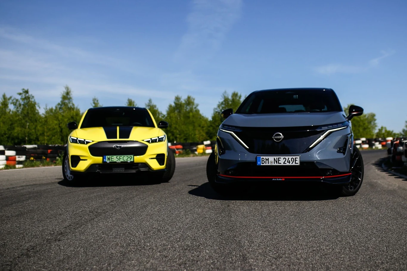 Dwa samochody elektryczne na torze wyścigowym, jeden w kolorze żółtym, drugi w kolorze szarym, wokół zielona roślinność i niebieskie niebo.