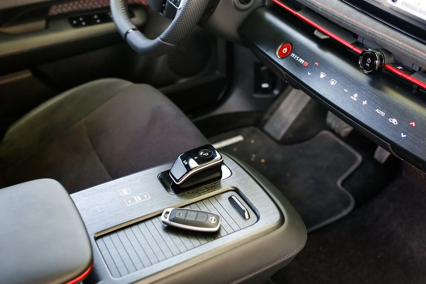 Wnętrze samochodu z nowoczesną konsolą środkową wyposażoną w uchwyt na filiżankę, schowek na kluczyk oraz eleganckie wykończenia. Na siedzeniu leży kluczyk do auta.