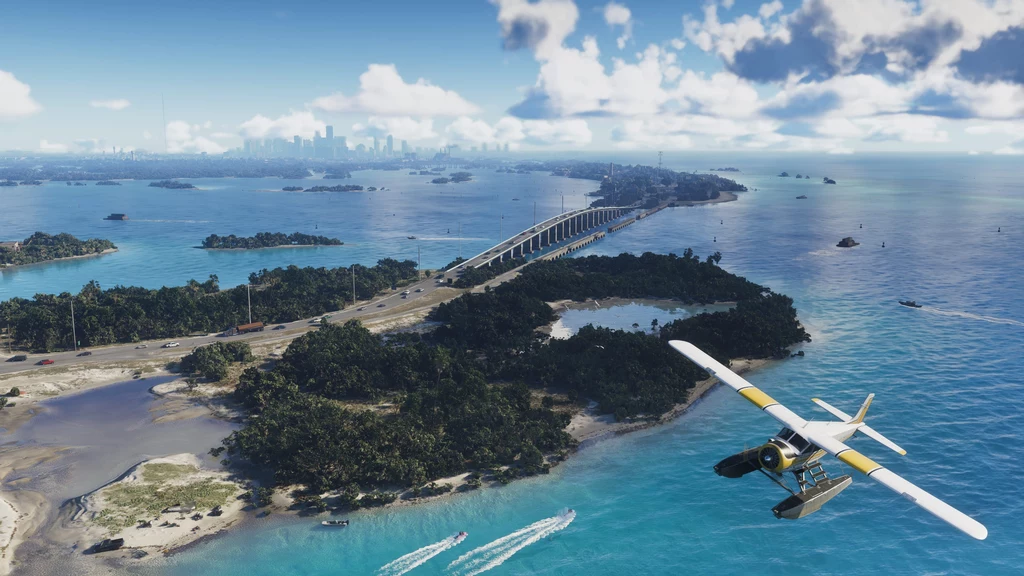 GTA VI zachwyca grafiką. Samolot w locie nad błękitnymi wodami i zielonymi wyspami, z mostem prowadzącym przez morze w tle. W oddali widoczna jest panorama miasta na horyzoncie, a poranne niebo pokryte lekkimi chmurami potęguje malowniczość krajobrazu.