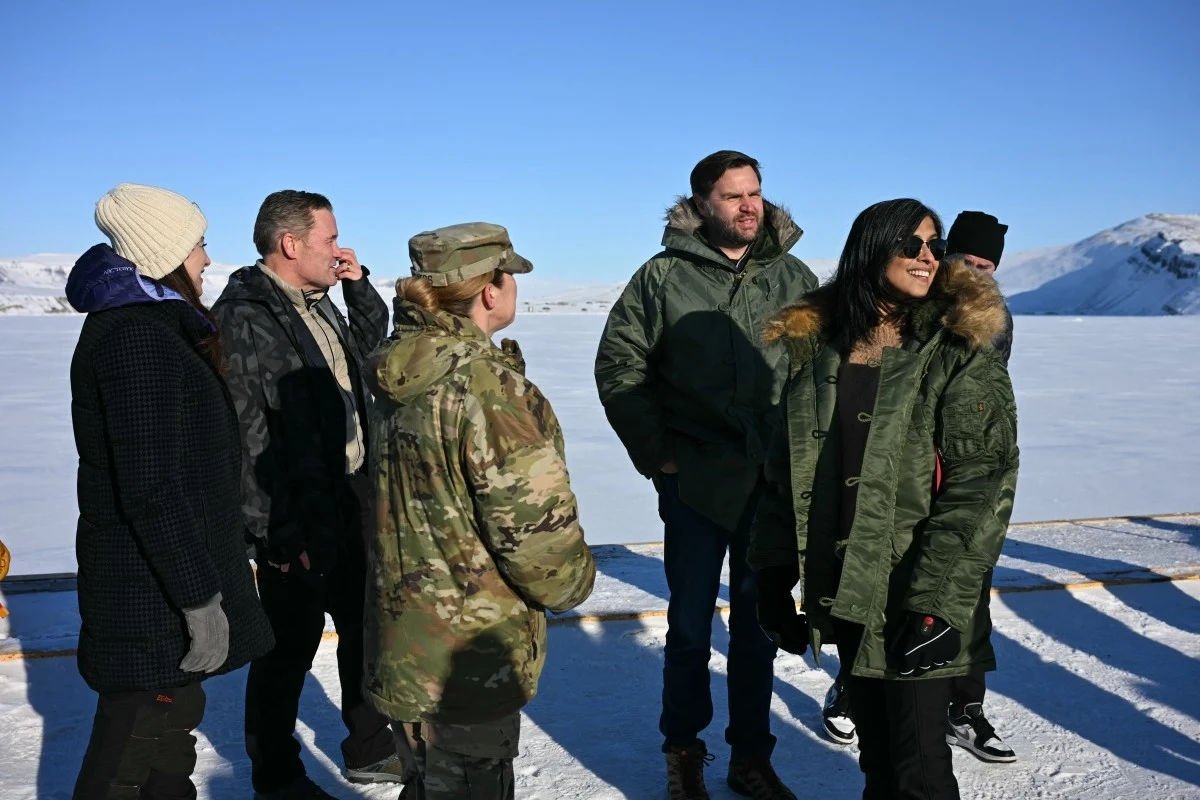 W marcu na Grenlandię udał się z wizytą wiceprezydent USA J.D. Vance Grupa ludzi stoi na śnieżnej scenerii, ubrana w ciepłe zimowe kurtki. Jeden z mężczyzn ma na sobie wojskową kurtkę. Za nimi rozciąga się górzysty krajobraz pokryty śniegiem pod błękitnym niebem.