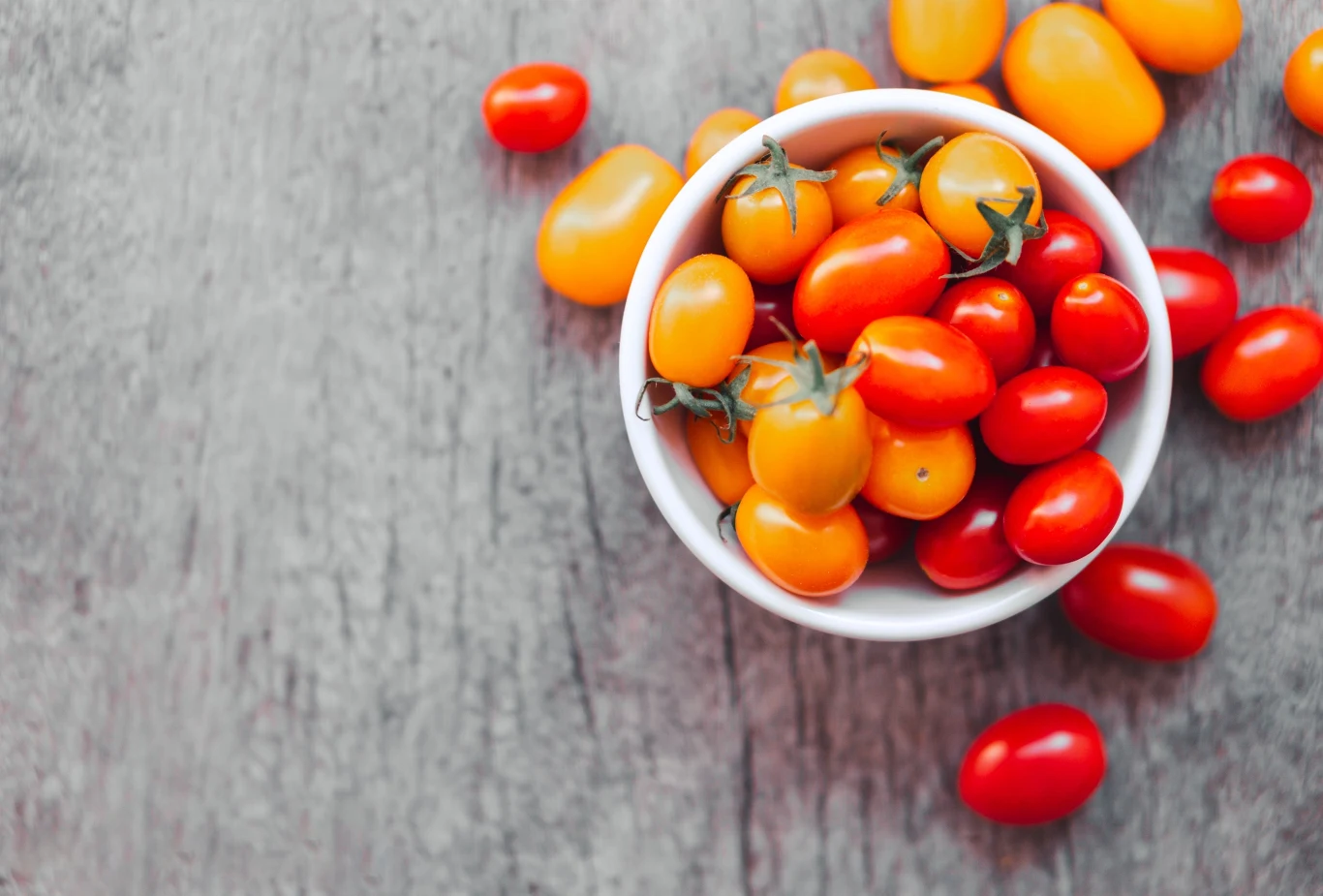Miska z czerwonymi i żółtymi pomidorkami koktajlowymi na drewnianej powierzchni, które tworzą barwną kompozycję.