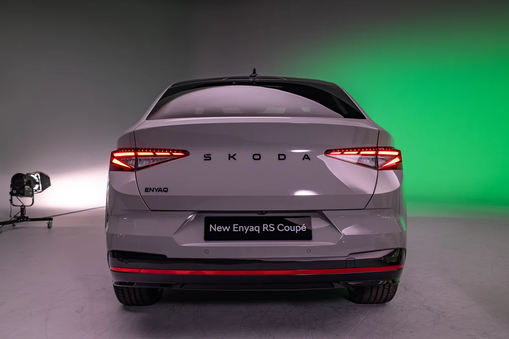 Odblaskowy pasek na tylnym zderzaku to element charakterystyczny dla wariantów RS. Nowoczesny samochód Skoda Enyaq RS Coupé z widocznymi, charakterystycznymi tylnymi światłami i eleganckim designem. Tło w studiu oświetlone na zielono.