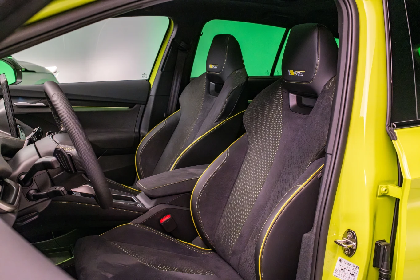 Wnętrze sportowego samochodu z czarnymi, wyprofilowanymi siedzeniami z żółtymi akcentami, skórzana kierownica i panel sterowania. Tapicerka i wykończenie wnętrza podkreślają sportowy charakter pojazdu.