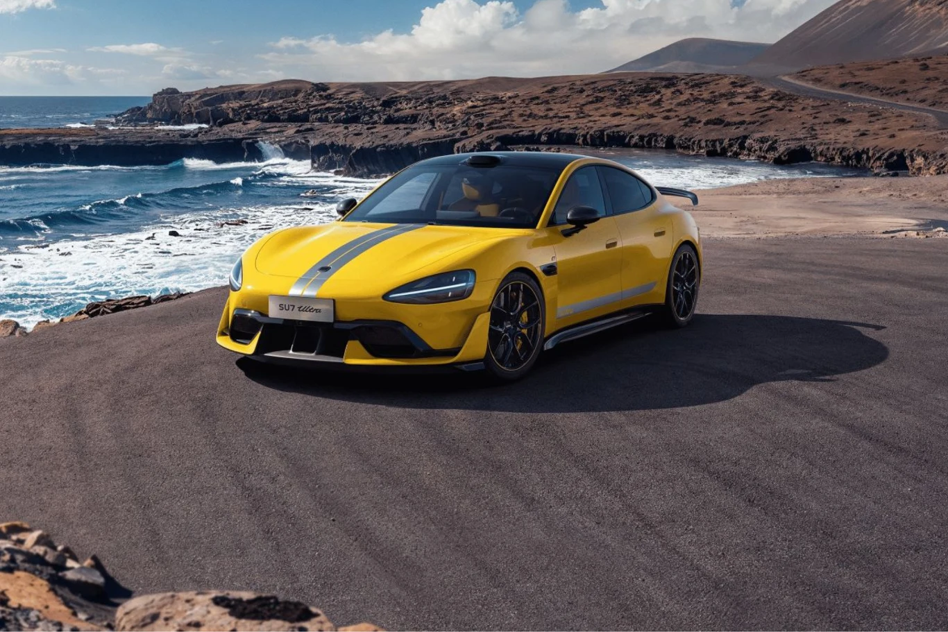 Xiaomi SU7 Ultra posiada trzy jednostki napędowe o łącznej mocy 1 548 KM. Żółty, sportowy samochód zaparkowany w malowniczej scenerii nadmorskiej z wijącą się drogą w tle i wzgórzami na horyzoncie.
