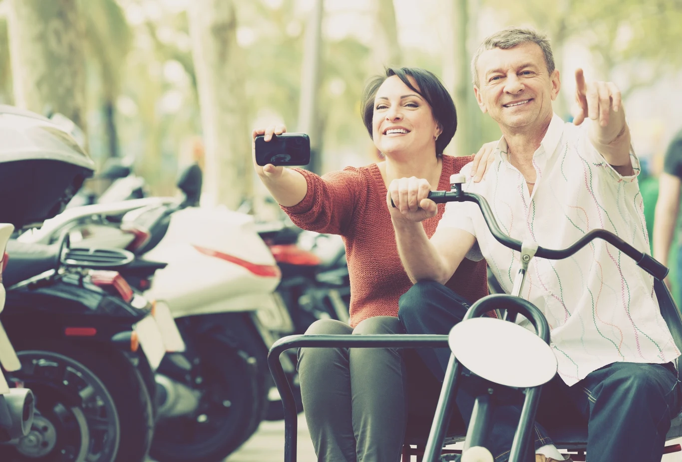 Szczęśliwa para robiąca sobie zdjęcie na tandemie, w tle widoczne parkujące motocykle.