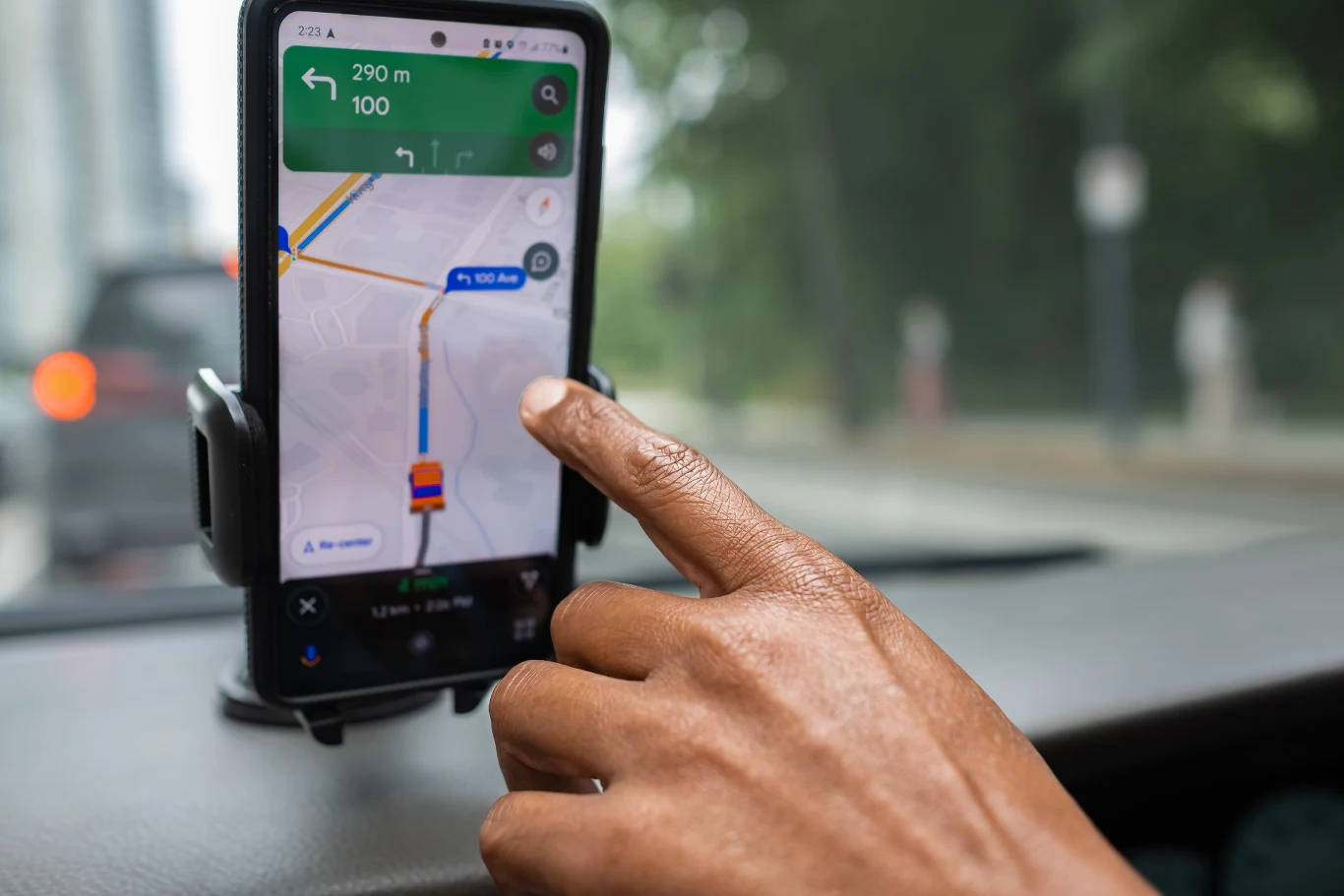 3 aplikacje, które pomogą obniżyć średnie spalanie samochodu. Ręka trzymająca smartfon z aplikacją nawigacyjną na mapie, zamontowany w uchwycie na desce rozdzielczej samochodu.