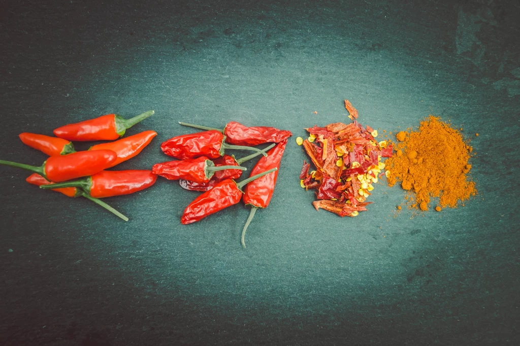 Papryczki chilli to prawdziwy sprzymierzeniec zdrowia Papryczki chili w różnych formach na ciemnym tle, w tym świeże, suszone i w postaci proszku. Kompozycja pokazuje różnorodność form, w jakich można używać chili.
