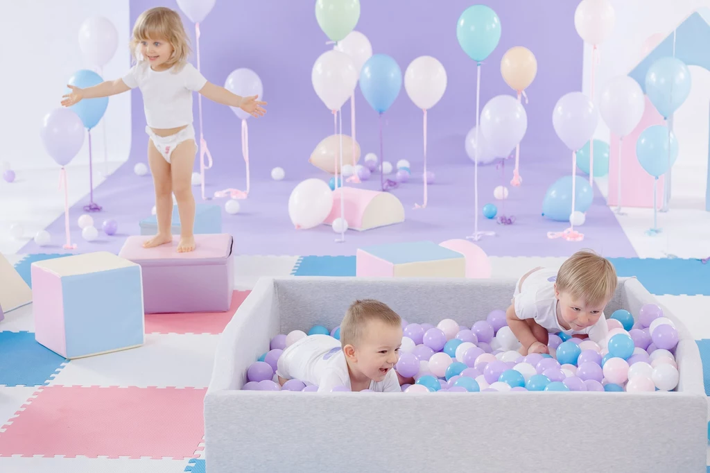 Pieluszki Happy Soft&Delicate zostały stworzone tak, by nie naruszać mikrobiomu, czyli naturalnej warstwy ochronnej skóry Dwoje dzieci bawi się w basenie z kolorowymi piłkami, trzecie stoi na pastelowym bloku, otoczone balonami i miękkimi matami, tworząc przyjazną atmosferę zabawy.