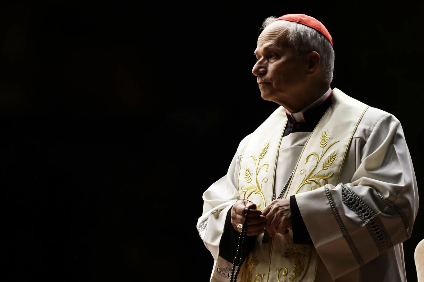 Kardynał Robert Prevost Duchowny w stroju liturgicznym, w tle ciemne tło, kontrastujące z jasną szatą i czerwonym biretem.