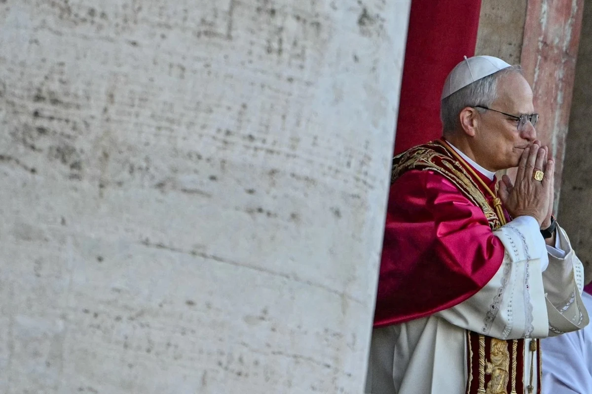 Osoba ubrana w tradycyjne religijne szaty modli się, stojąc na tle kamiennych ścian i czerwonej zasłony.