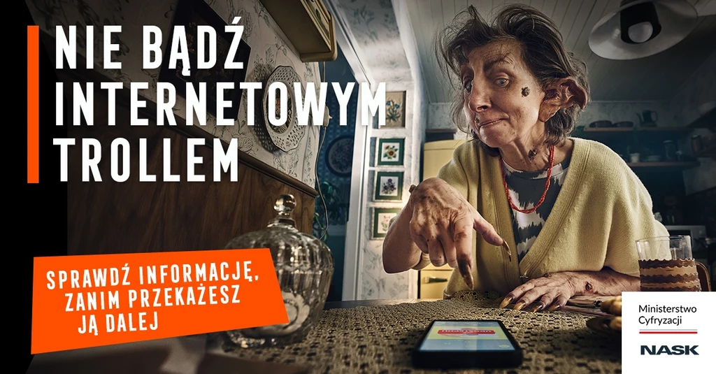 Kampania MInisterstwa Cyfryzacji i NASK. Kobieta w pomieszczeniu wskazuje na telefon leżący na stole. Obok niej znajduje się szkatułka. Obrazek zawiera hasło 'Nie bądź internetowym trollem' i logo Ministerstwa Cyfryzacji i NASK.