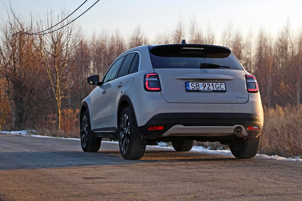 W stylizacji Fiata 600 dominują krągłości Samochód typu SUV w kolorze szarym stoi na szosie. W tle widać drzewa bez liści, co sugeruje porę jesienno-zimową. Auto ma tablicę rejestracyjną, a wokół rozciąga się wiejska sceneria.