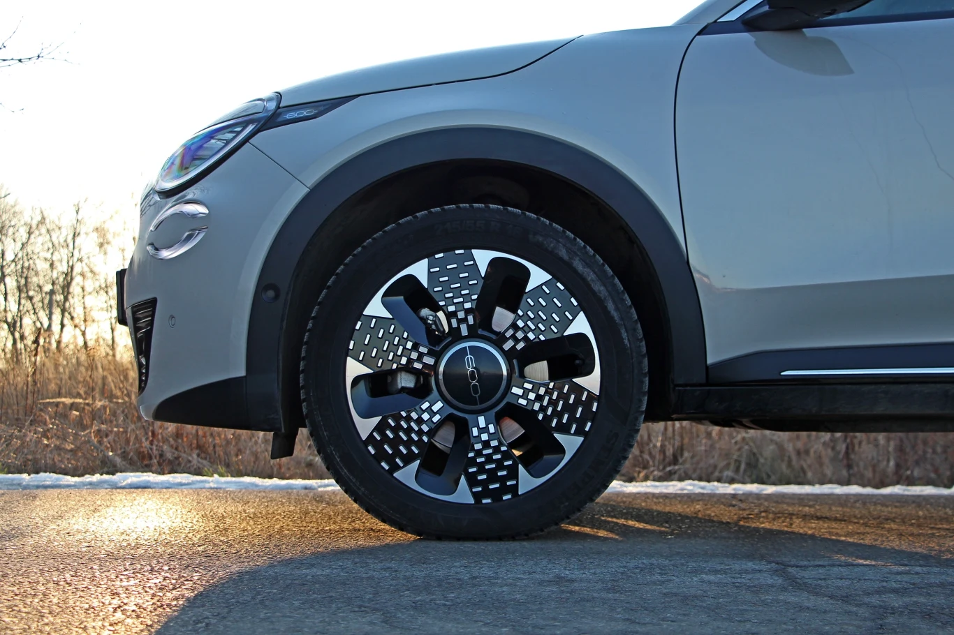 Bok szarego SUV-a z nowoczesnym designem felgi na tle spokojnego krajobrazu o zachodzie słońca.