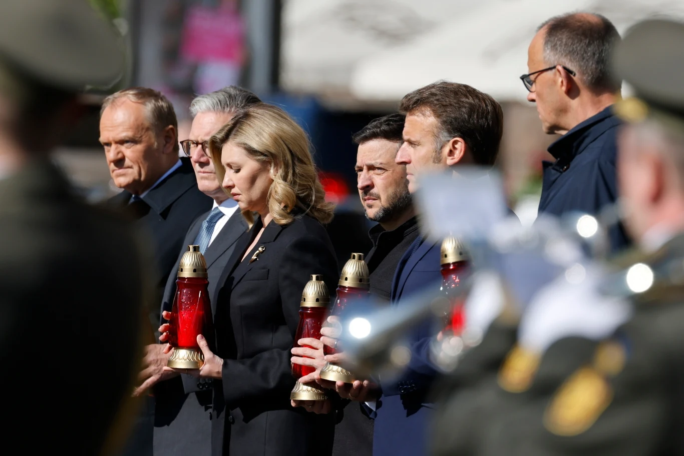 Liderzy "koalicji chętnych" na kijowskim Majdanie Grupa osób ubranych w ciemne stroje w trakcie oficjalnej ceremonii, każdy z nich trzyma znicz. W tle widoczni są żołnierze oraz niewyraźne elementy architektury.