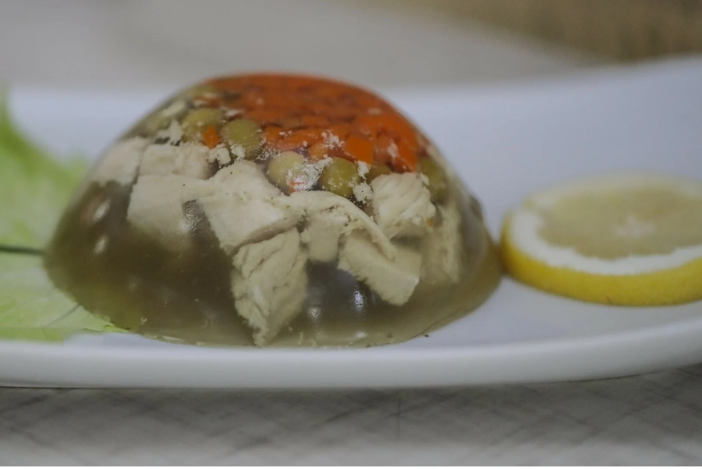 Galaretka z kurczakiem i warzywami podana na talerzu obok plasterka cytryny.