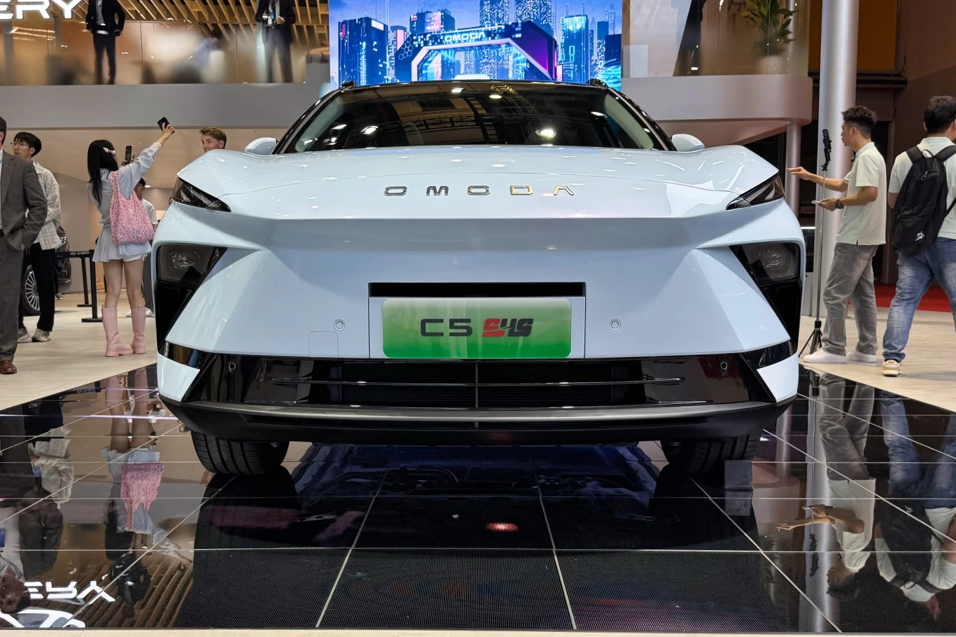 Nowoczesny samochód elektryczny Omoda C5 EV w kolorze białym prezentowany na wystawie motoryzacyjnej, otoczony przez odwiedzających.