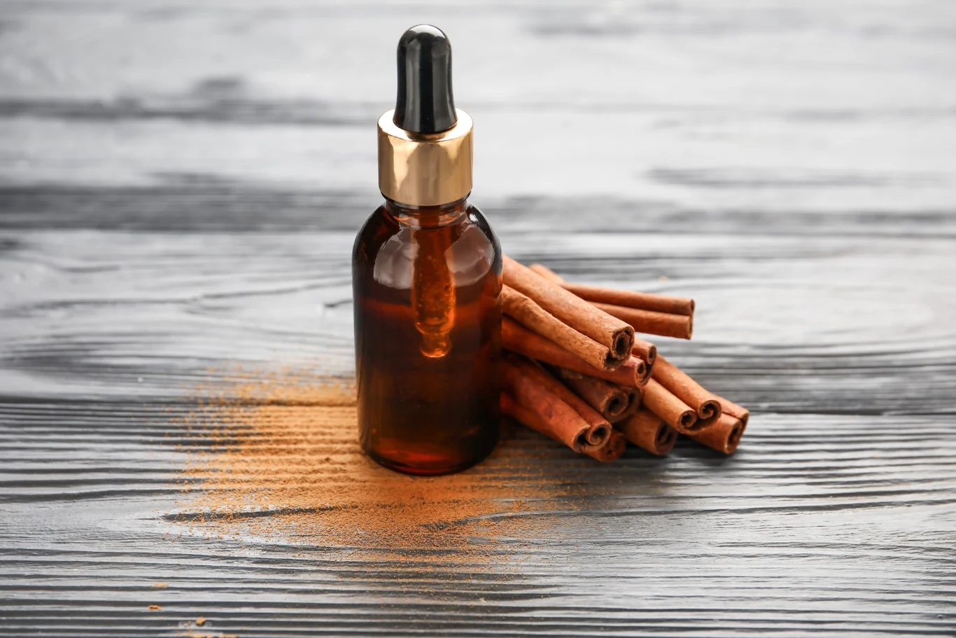 Olejek cynamonowy jest uważany za bezpieczny. Butelka z ciemnego szkła z pipetą stoi obok laski cynamonu na drewnianym tle, otoczona odrobiną rozsypanego cynamonu w proszku.